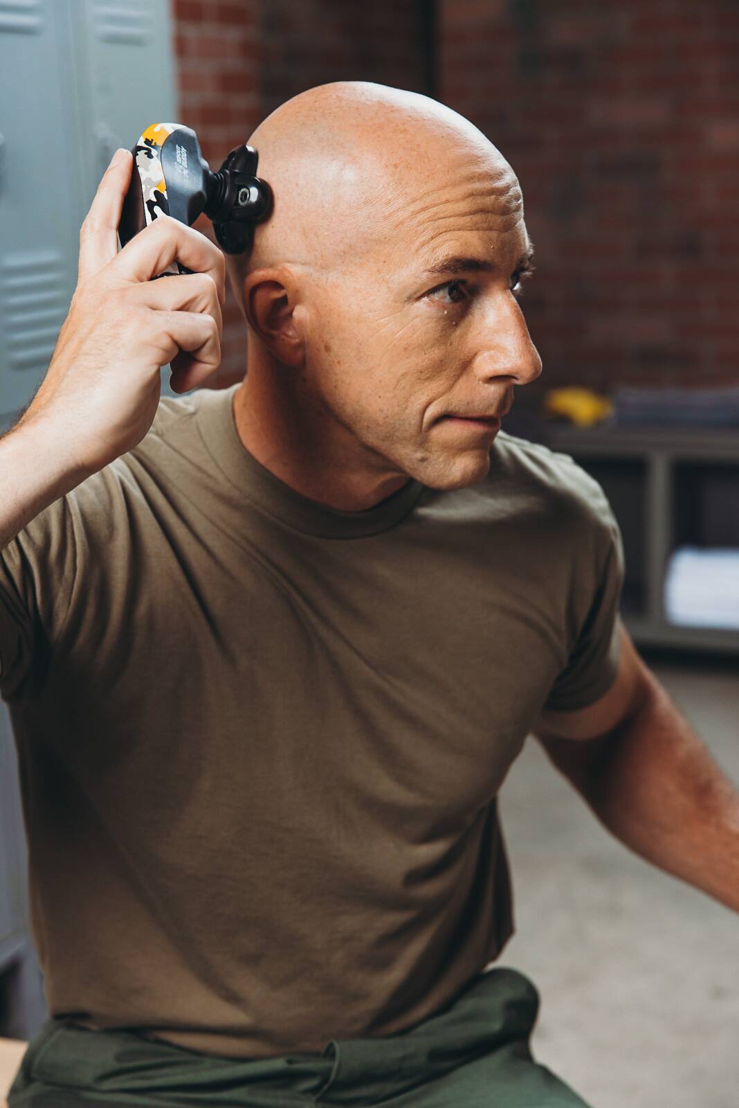 bald man in a locker room using a bald shaver to maintain military grooming standards