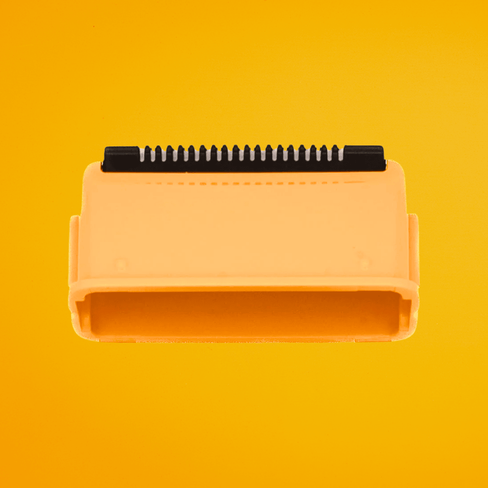 Close-up view of an orange Cut Buddy precision trimmer attachment with a black serrated edge on a yellow background.